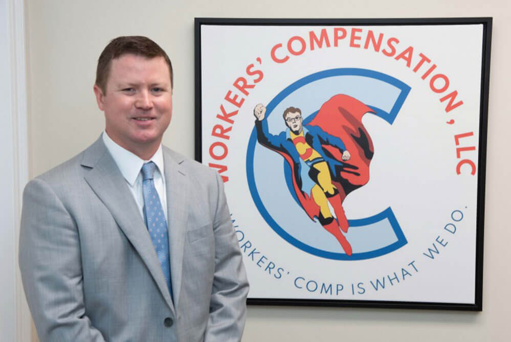 A Workers' Comp LLC attorney, Corey Fitzpatrick, posing in front of the company logo.